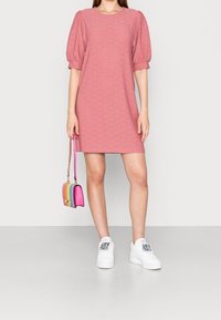 Vaaleanpunainen lyhythihaisessa mekossa, jossa on tekstuuri, puffihihat ja rento leikkaus, yhdistetty valkoisiin tennareihin ja pieneen moniväriseen käsilaukkuun.