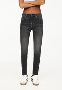 Jeans neri skinny con un design a vita media, dotati di tasche anteriori e cuciture tonali, abbinati a sneakers bianche con rifiniture nere.