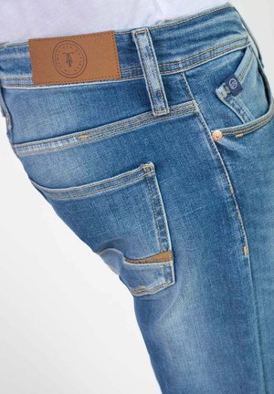 Jean en denim bleu clair avec un patch de ceinture en cuir brun, cinq poches, coutures orange et une coupe slim.