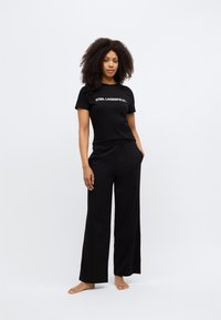Set negru de haine de relaxare format dintr-un tricou mulat cu logo și pantaloni largi, cu croială lejeră. Material moale și talie elastică pentru confort.