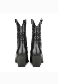 Botines de tacón bajo de imitación cuero negro con punta afilada, costuras decorativas y cierre de cremallera en la parte trasera.