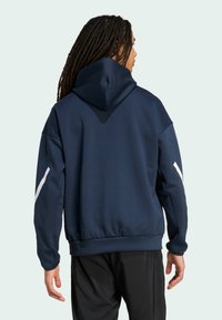 Sudadera azul marino con cuello alto y capucha ajustable. Presenta acentos blancos en las mangas y un corte relajado. Textura suave.