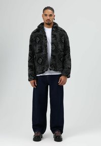 Zachte jas met een zwart-grijs patroon en een kraag, gecombineerd met losse donkere spijkerbroeken en zwarte schoenen met roze veters. Daaronder een effen wit T-shirt.