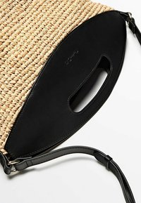 Borsa tote di paglia intrecciata con base in pelle nera. Presenta una forma arrotondata, un manico a taglio e una tracolla staccabile.