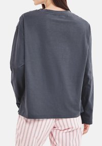 Långärmad, mörkgrå skjorta med rund halsringning; slät textur; använd med randiga pyjamasbyxor i rosa och vitt.