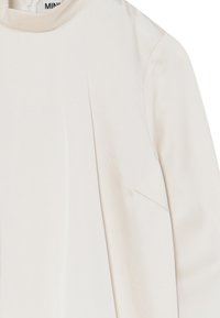 Lys beige langærmet bluse med høj halsudskæring. Har en glat tekstur, diskret syninger og en afslappet pasform.