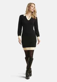 Robe pull noire avec décolleté en V, col et poignets crème. Présente un ourlet côtelé et une bande contrastante crème clair en bas.