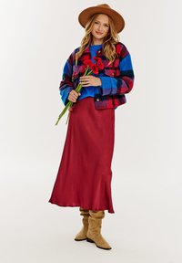 Kolorowa kratkowana kurtka w niebieskim, czerwonym i czarnym kolorze, na niebieskim swetrze. Czerwona satynowa spódnica maxi z rozszerzanym dołem, w połączeniu z beżowymi botkami sięgającymi do kolan.