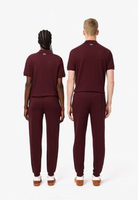 Burgundy matchande kortärmad skjorta och byxor, tillverkade av mjukt tyg, med elastiska ärmslut och en logotypdetalj på kragen.