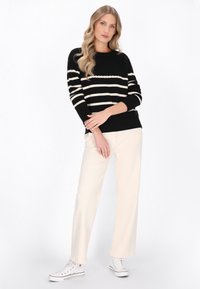 Maglione a righe bianche e nere con un motivo di maglia testurizzata, abbinato a pantaloni a gamba larga color crema e sneakers bianche. Vestibilità e design casual.