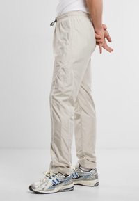 Beige sportieve broek met een elastische tailleband en trekkoord. De zijnaad heeft witte piping. Gedirigeerd met zilver en blauwe sneakers.