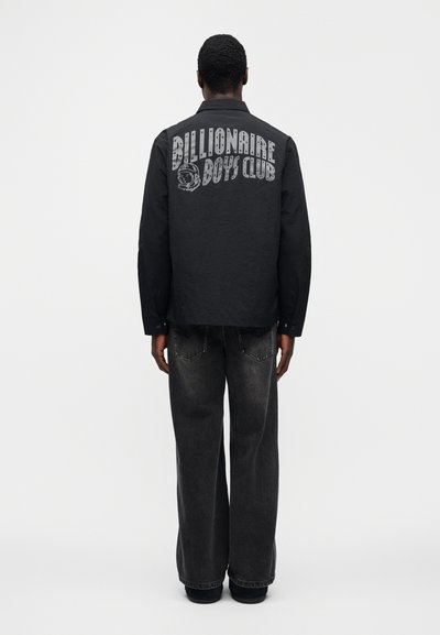 Μαύρο μακρυμάνικο πουκάμισο με το λογότυπο «Billionaire Boys Club» εκτυπωμένο στην πλάτη. Συνδυασμένο με άνετο σκούρο τζιν, μινιμαλιστικός σχεδιασμός.