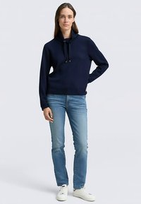 Granatowa bluza z kapturem z troczkami, długimi rękawami i krótkim krojem, zestawiona z jasnoniebieskimi dżinsami i białymi trampkami.