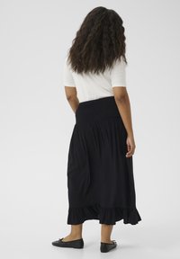 Black, ruffled maxi skirt with a stretchy, smocked waistband. Worn with a white fitted top and black flat shoes. The fabric is lightweight.