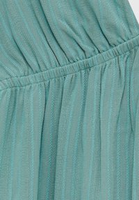 Tyrkysová látka s vertikálními pruhy a texturovaným povrchem. Obsahuje nařasený elastický pas a kontrastní stehy v světle modré barvě.