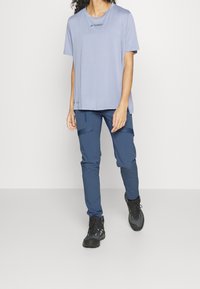 Ljuslila kortärmad T-shirt med rundad hals och "TERREX"-logotyp; ihopparad med mörkblå cargobyxor och svarta vandringskängor.