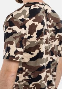Bomullströja i ett kamouflage-mönster med nyanser av brunt, grönt och svart. Korta ärmar och en klassisk rund halsdesign.