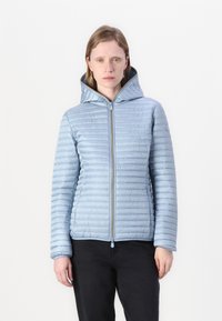 Lichtblauw pufferjack met horizontale quilt, een aansluitende capuchon, rits aan de voorkant en een zachte glans. Draag met zwarte broek.