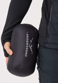 Black, lightweight packing bag with a smooth texture, featuring the "SWEDEMOUNT" logo in white. Held in a hand, with a compact, cylindrical shape.