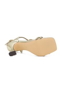 Sandale en métal doré avec un design à lanières texturé, un talon moyen bloc et une semelle beige lisse. Dotée de lanières tressées et d'une fermeture autour de la cheville.