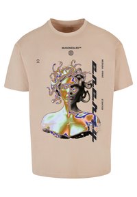 Béžové tričko s grafikou Medúzy, která má živé, deformované barvy a černé textové akcenty na bocích. Krátké rukávy a kulatý výstřih.