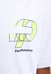 Tricou alb din bumbac cu un design grafic, având un „P” galben neon și accente cu carouri, alături de textul „Petrol Industries” în negru.