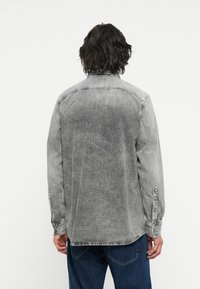 Grijze spijkerblouse met een vervaagde afwerking, knoopmanschetten en een rechte zoom. Heeft een relaxte pasvorm en een zachte textuur.