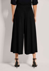 Zwarte wijde broeken met een rekbare tailleband, een gladde textuur en een enkel-lange snit, gecombineerd met zwarte hoge hakken.