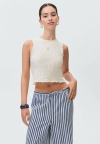 White textured crop top with a scalloped hem, paired with blue and white striped wide-leg pants. Accessories include a dark bracelet.