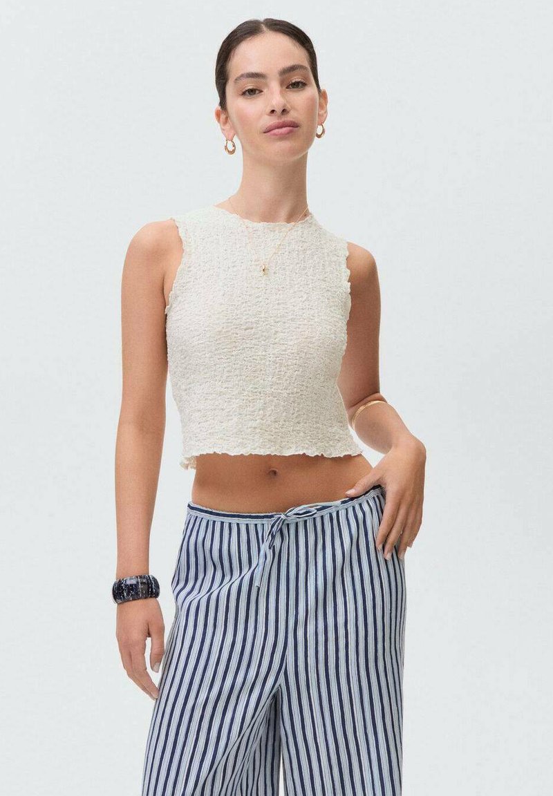 White textured crop top with a scalloped hem, paired with blue and white striped wide-leg pants. Accessories include a dark bracelet.