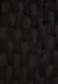 Černá texturovaná tkanina se šachovnicovým vzorem a třásněmi, vytvářející vrstvený vzhled s různými hloubkami a zajímavostí povrchu.