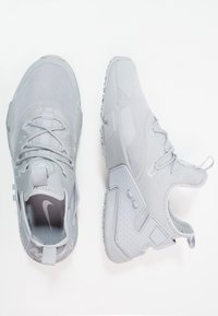 Ljusgrå sportskor med ovandel i mesh, rundad tå, gummisula, distinkt häldesign och subtil märkning på tungan.