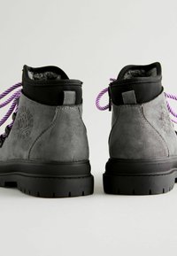 Bottines en suede grises avec des accents noirs, dotées de lacets violets et d'une semelle texturée, conçues pour la durabilité et le confort.