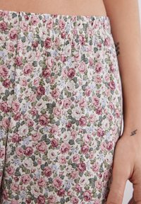 Bloemige pyjamabroek met een aansluitende tailleband; featuring roze, paarse en groene rozen op een lichte achtergrond, met een gestructureerd stoffenpatroon.