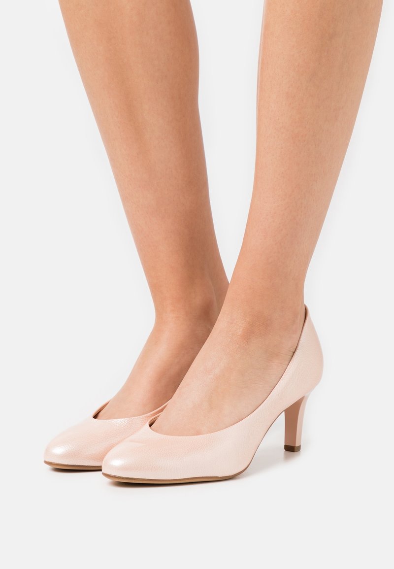 Zapatos de tacón alto de cuero rosa claro con punta redondeada y un tacón bajo en bloque. El acabado texturizado en la parte superior añade detalle. Curvatura sutil en el talón.