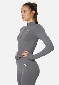Gray athletic zip-up jacket featuring long sleeves, a high collar, and a fitted design, paired with matching high-waisted leggings.