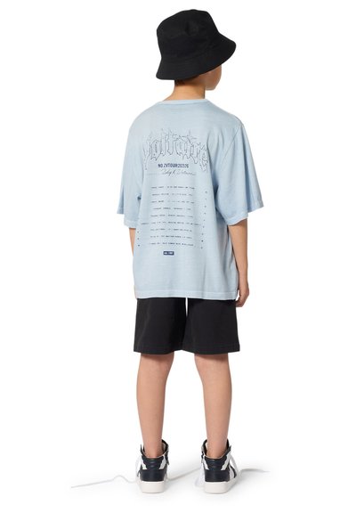 T-shirt bleu clair oversize avec imprimé graphique au dos, associé à un short noir et des baskets montantes. Un bob noir complète le look.