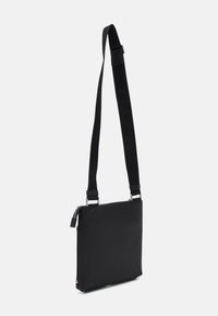 Sac messager noir au design épuré, fabriqué en tissu lisse. Doté d'une bandoulière réglable et de quincaillerie en argent, avec une fermeture zippée.
