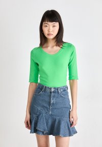 Haut côtelé vert à manches longues avec un col arrondi, associé à une jupe en denim bleu dotée d'un ourlet à volants évasés et de détails à bord brut.