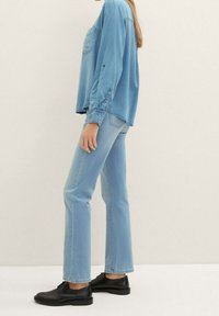 Camisa de mezclilla azul claro con mangas largas y un bolsillo en el pecho, combinada con jeans rectos azul claro y zapatos negros de cordones.