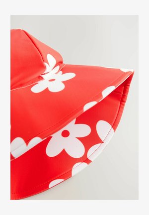 Piros kalap sima anyagból, nagy fehér virágmintákkal. A széle széles és lekerekített, kontrasztos varrással.