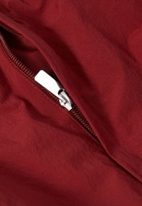 Tessuto rosso con una textura increspata presenta una cerniera argento parzialmente aperta, che rivela una fodera interna coordinata.