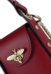 Sac bandoulière en cuir rouge avec une finition texturée, orné d'un motif d'abeille dorée et d'une sangle chaîne décorative.