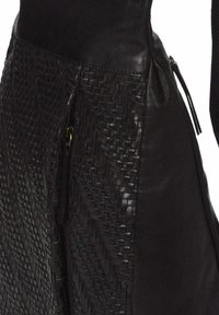 Prenda de cuero negro con panel de textura trenzada intrincada y una cremallera con tirador de cuero en el lateral.