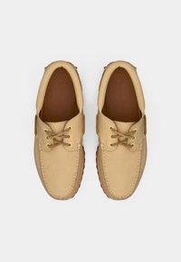 Beige bőr cipő, kerek orral, barna belső talppal, két arany fűzőlyukkal és világosbarna fűzővel. Gumitalp jellemzi, részletes varrással.