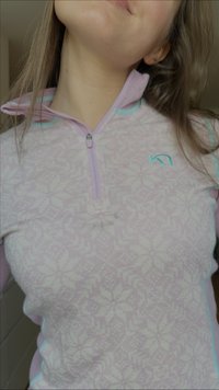 Pulôver rosa claro com fecho de correr e padrão de flocos de neve. Apresenta detalhes contrastantes em turquesa ao longo do zíper e dos punhos. Textura macia.