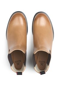 Brązowe skórzane mokasyny z zaokrąglonym noskiem, kontrastującymi ciemnymi elastycznymi bokami i teksturowaną wkładką. Posiadają małą czerwoną pętelkę na pięcie.