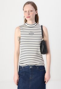 Bezranka dryžuota palaidinė šviesiai kreminės ir tamsiai mėlynos spalvos, su aukštu kaklu. Krūtinės srityje yra spausdinta "Tommy HILFIGER" logotipas. Tamsiai mėlyni džinsiniai sijonai ir juoda rankinė.