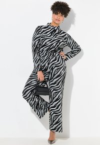 Zebra print jumpsuit in zwart en zilver met een hoge halslijn, lange mouwen en uitlopende benen. Inclusief een kleine zwarte handtas en grijze hakken.