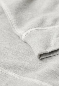 Tessuto grigio con una trama liscia, caratterizzato da cuciture bianche a contrasto lungo le cuciture e un bordo morbido e ripiegato.